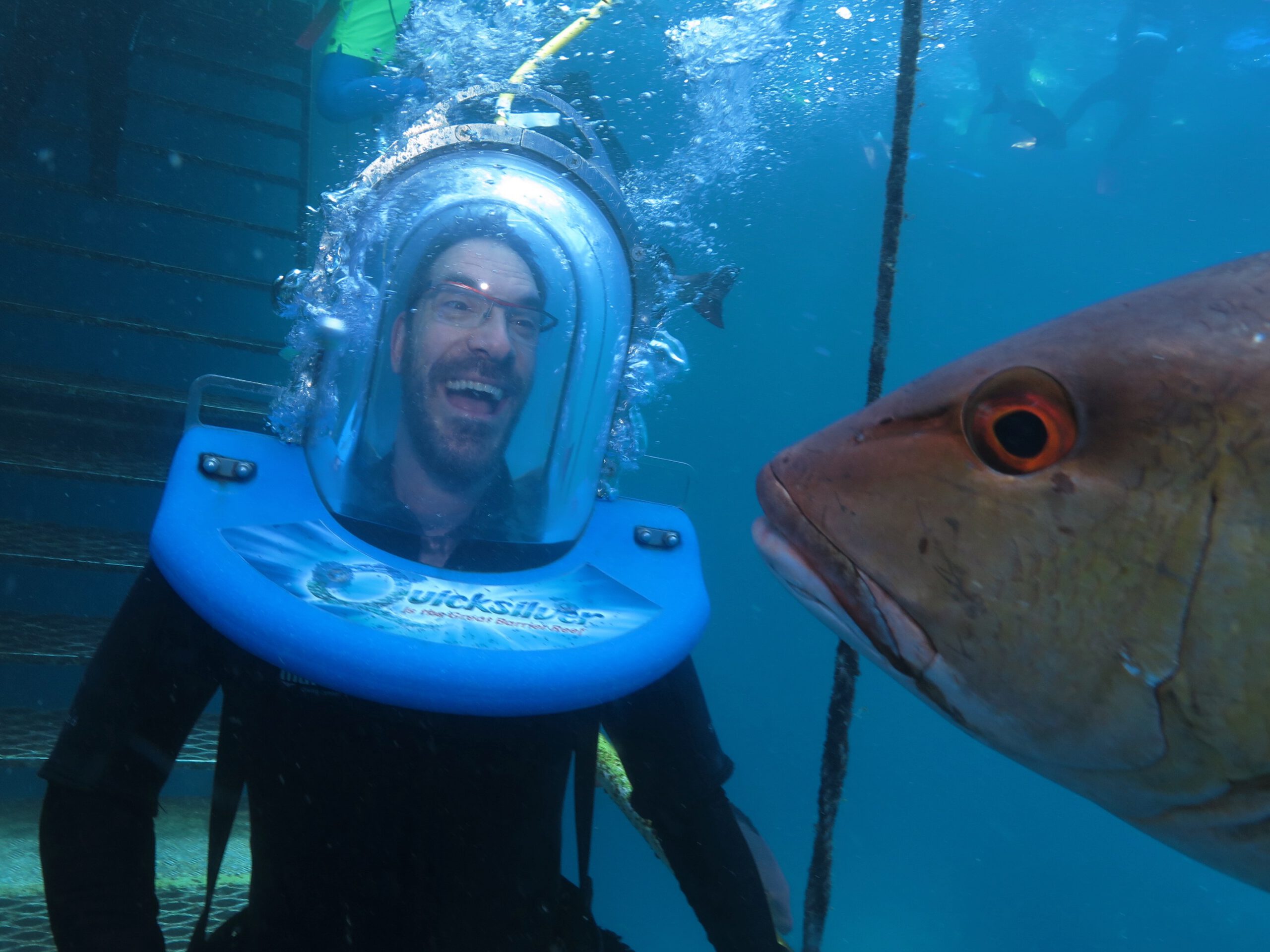 Etienne, our disability coach is walking underwater with a bell scuba helmet making him look like an alien from Mars arrack laughing. The fish is intrigued