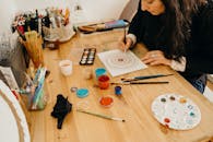 Artist painting a mandala design using various pigments and brushes indoors.