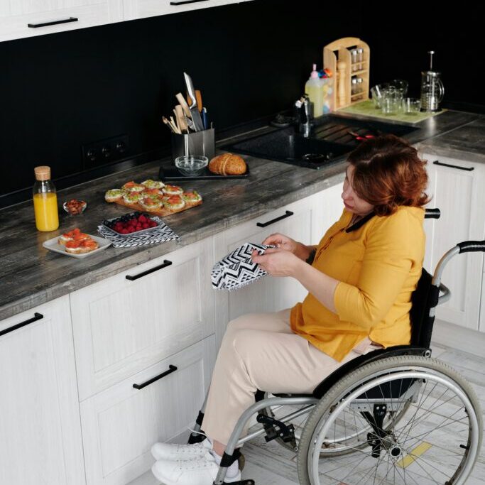 A woman in a wheelchair prepares lunch in a modern kitchen setting.